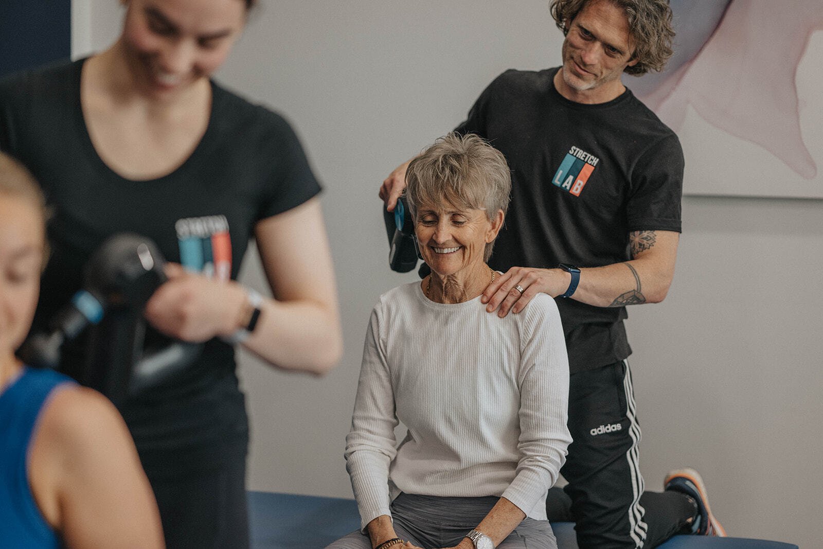 instructor using a muscle gun on a woman during a stretch class