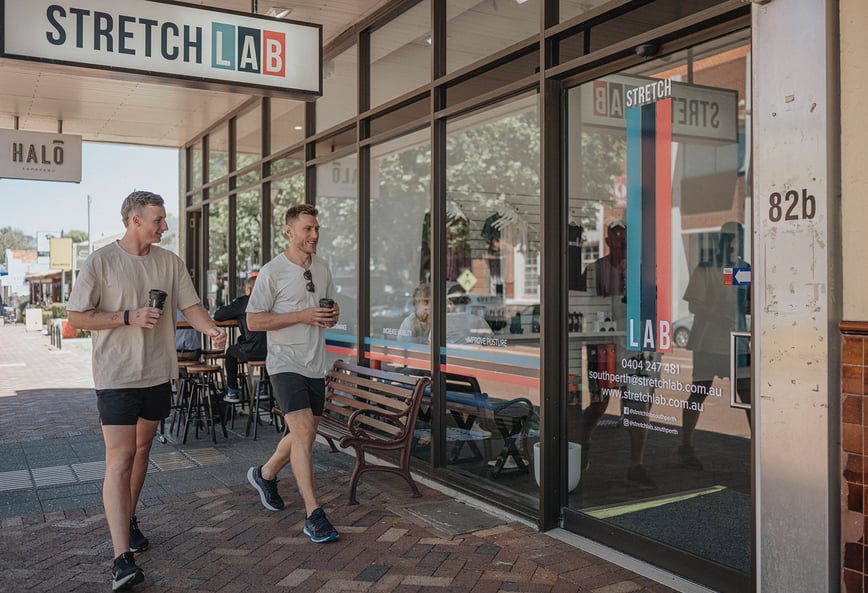 two men with coffees entering stretch lab to stretch before a run
